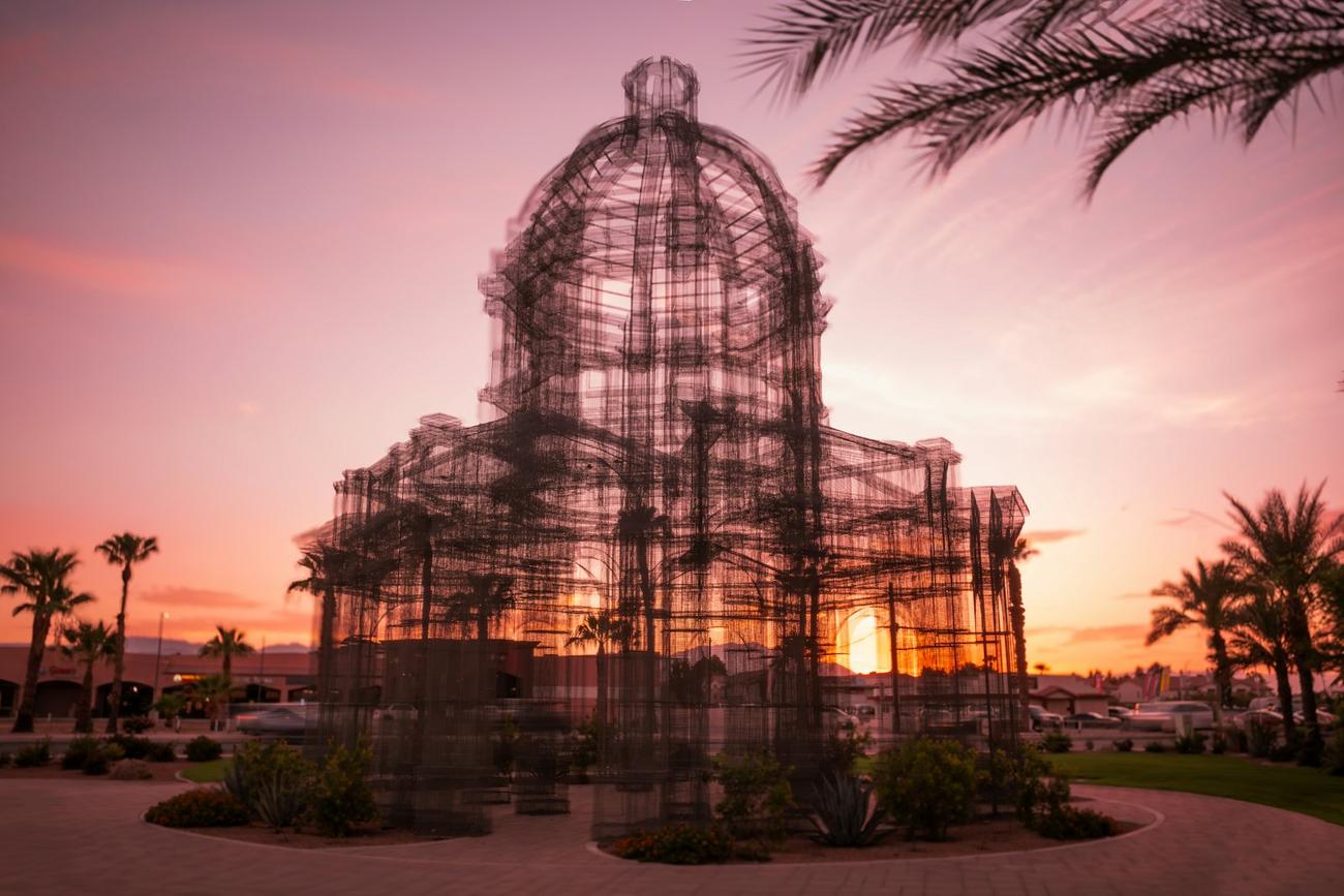 A wire sculpture of a building against a pink desert sunset